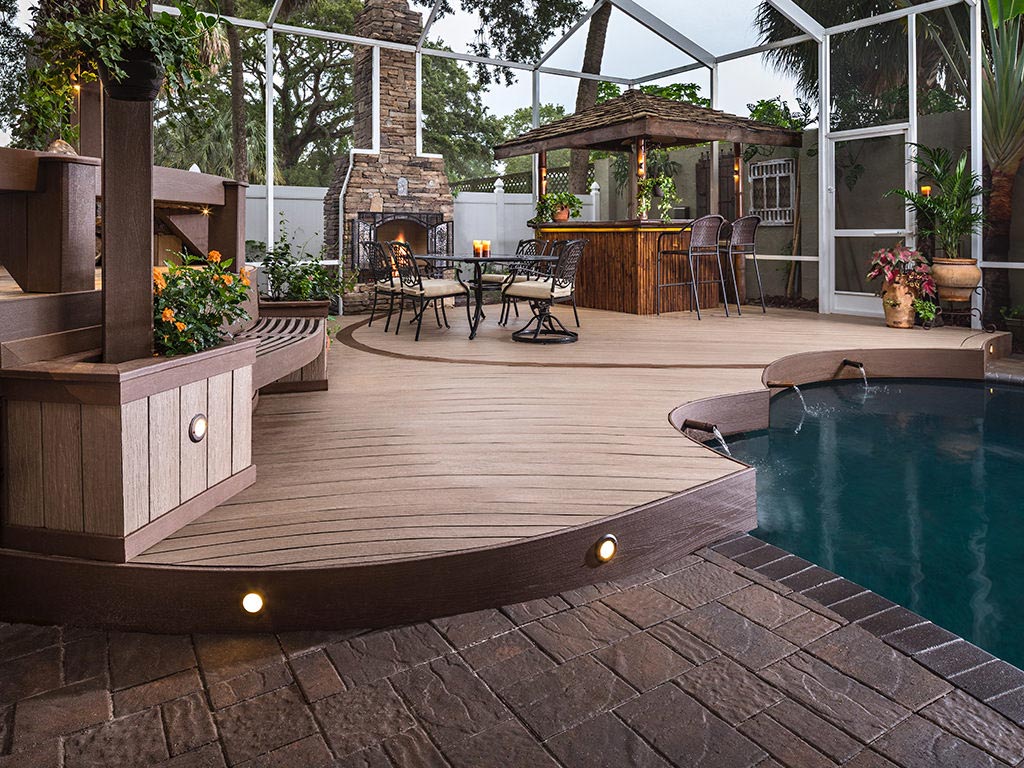 MoistureShield composite decking pool deck with built-in grilling station, outdoor fireplace, and bar.
