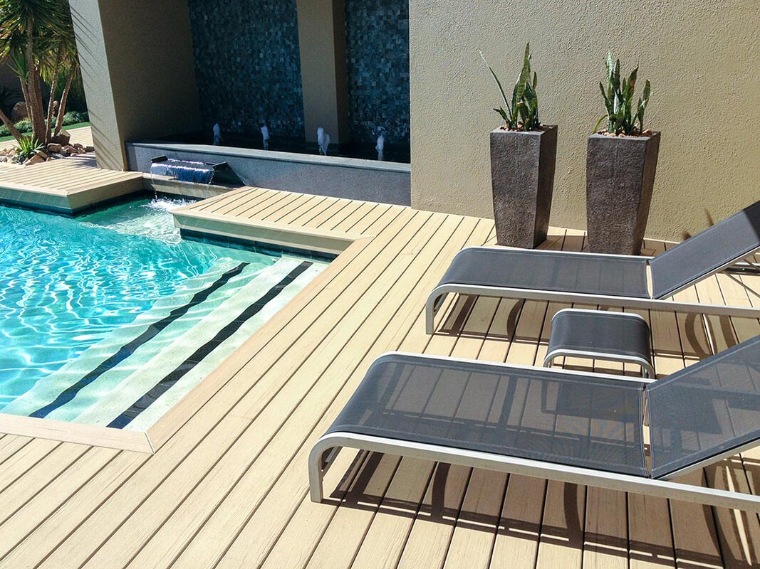 MoistureShield composite decking pool deck with stone planters, two deck chairs, and a wall fountain.