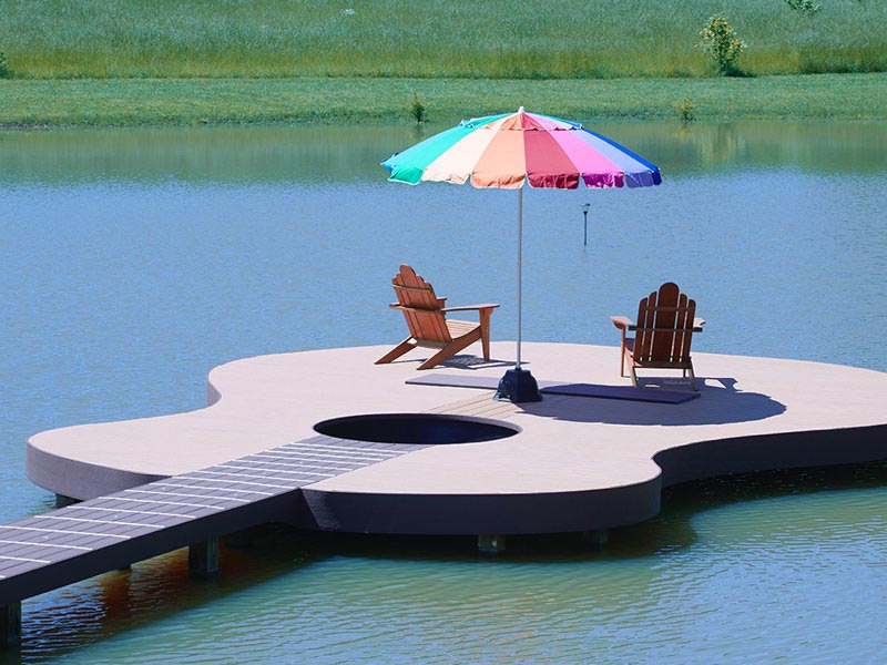 Guitar-shaped MoistureShield composite decking dock with patio chairs and an umbrella.