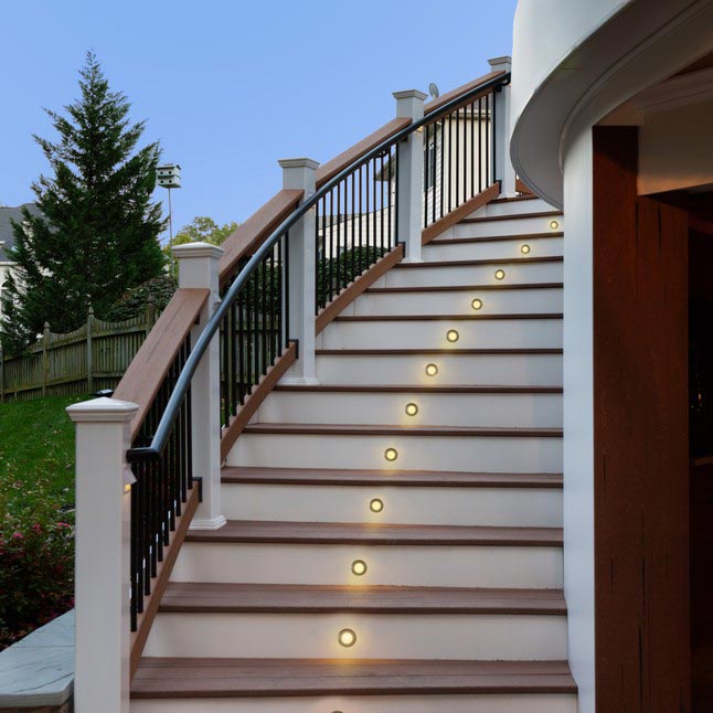 Close upward view of MoistureShield composite deck stair lighting on a curved set of white and brown stairs.
