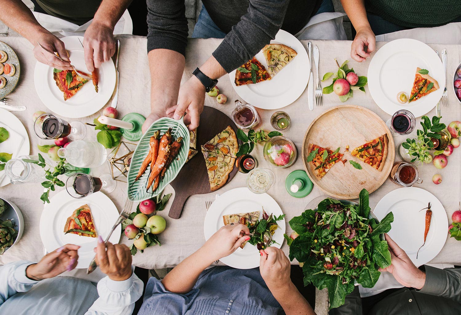 Overhead view of people serving themselves pizza and salad.