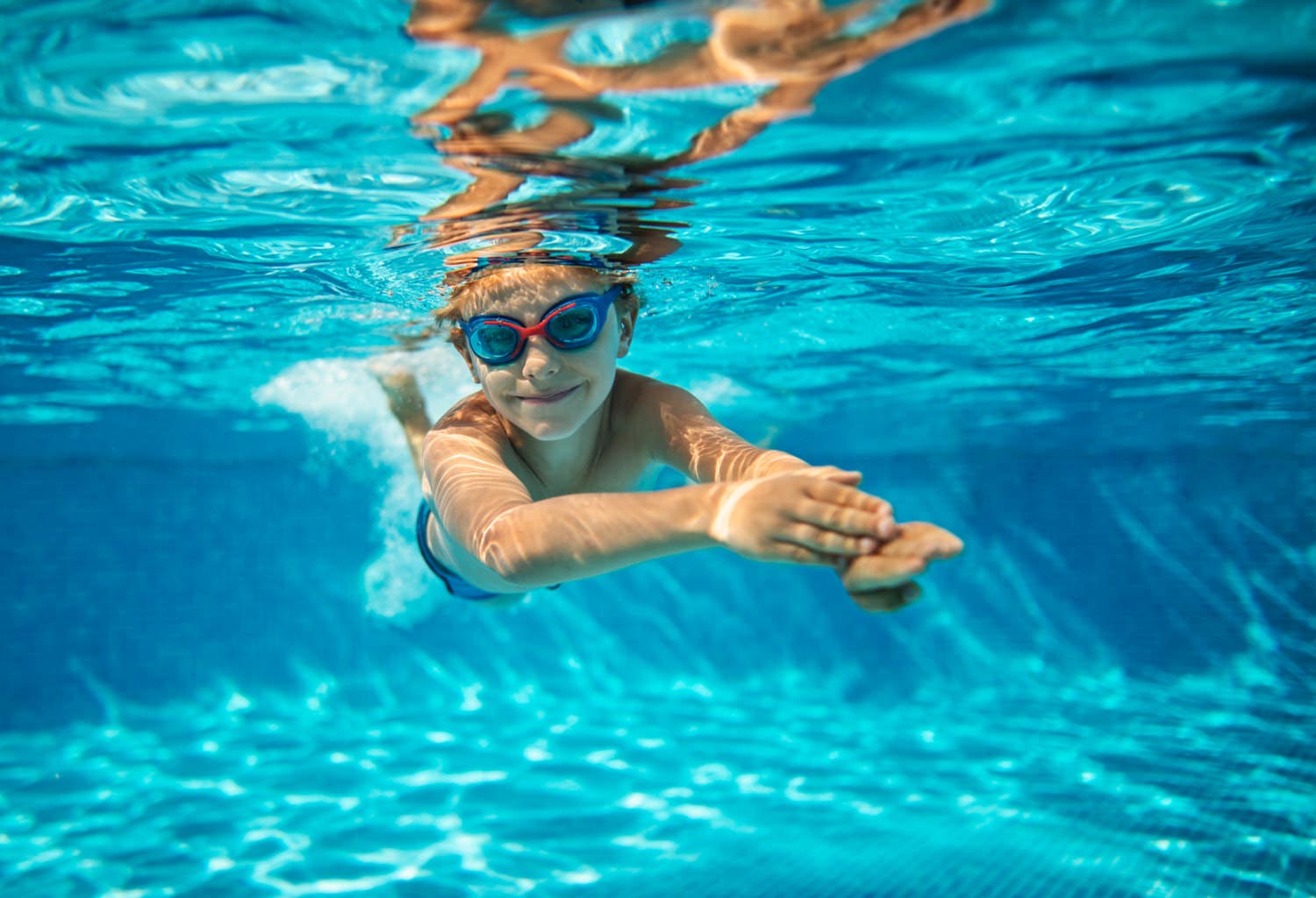 Underwater view of a child wearing goggles swimming in a pool.