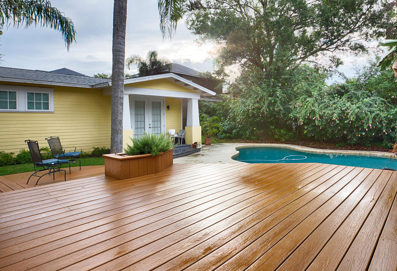 Yellow house with white trim and brown composite pool deck.