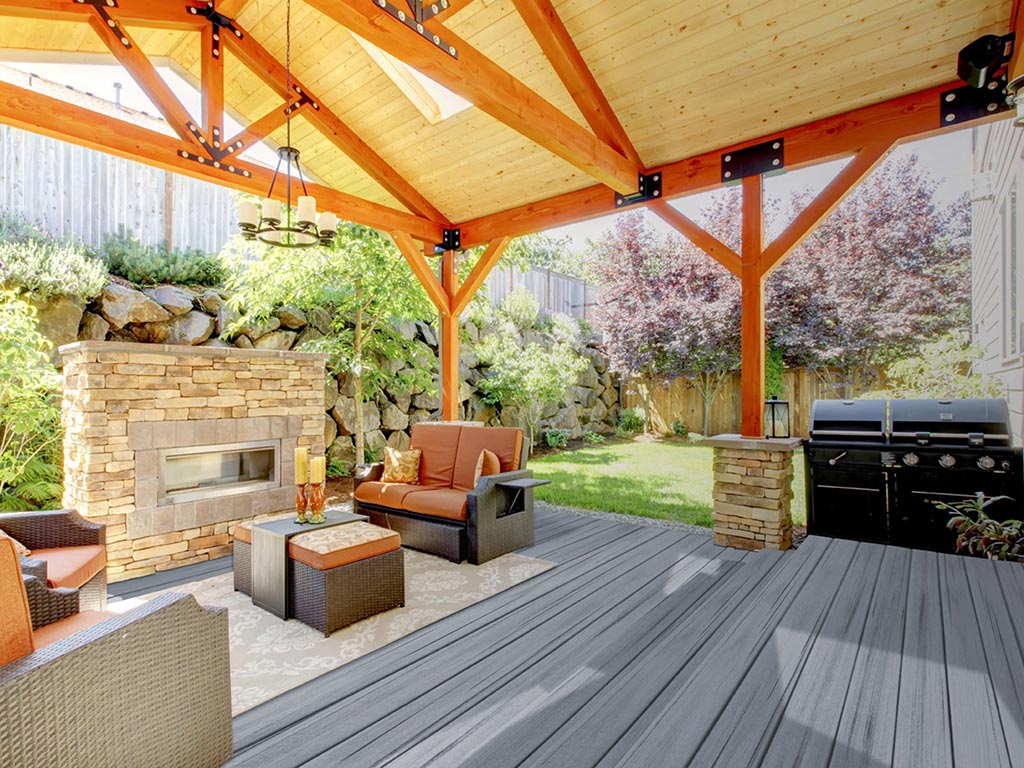 MoistureShield Elevate composite decking covered backyard patio with an outdoor fireplace, grilling area, and modern wicker conversation furniture set.