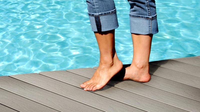 design-coolor Feet of a person standing on a composite pool deck featuring CoolDeck Technology.